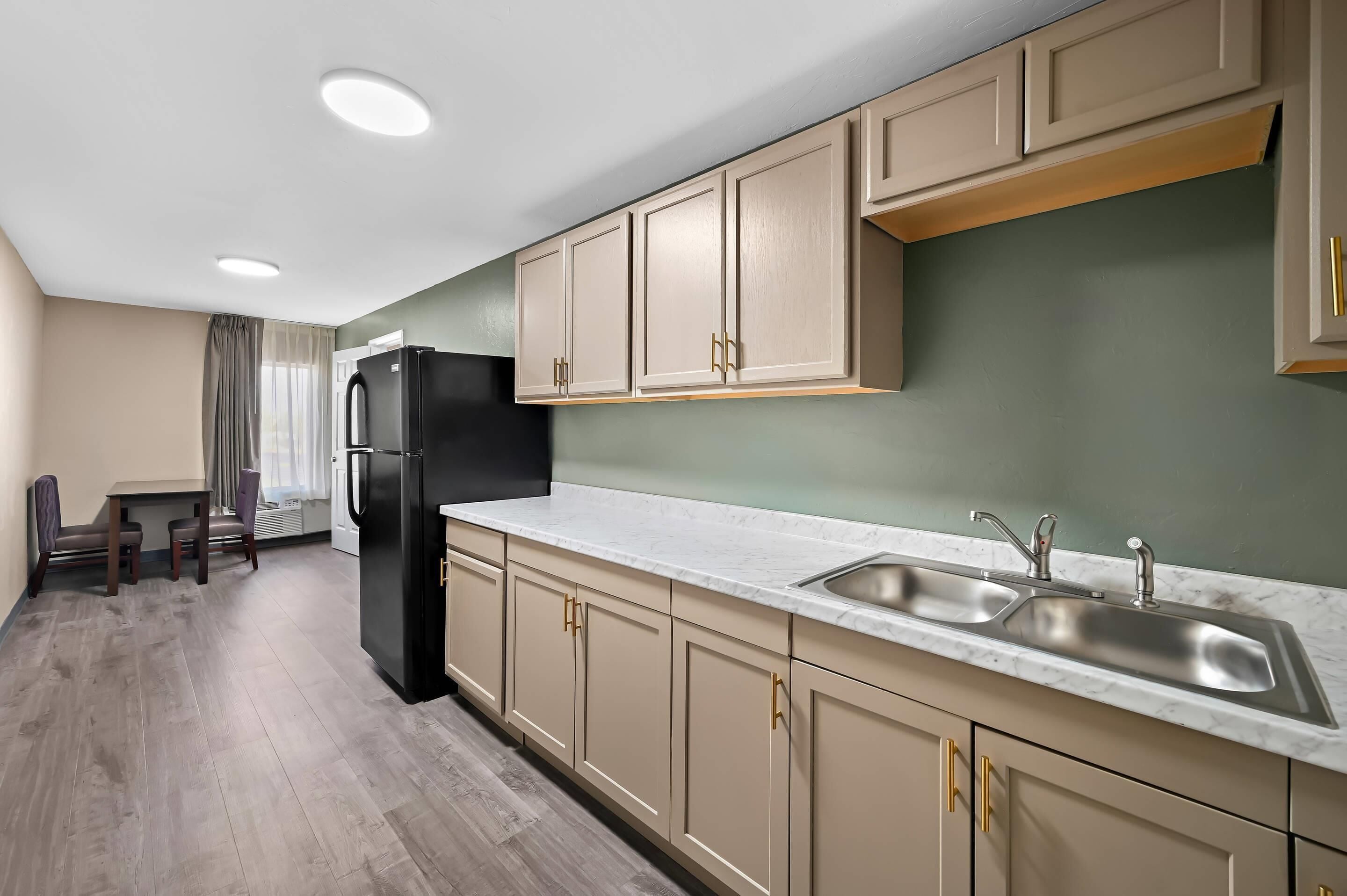 Una cocina moderna con armarios color beige, un refrigerador negro y una encimera de mármol.