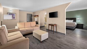A modern hotel room with a sofa, ottoman, flat-screen TV, bedside table, and a bed.