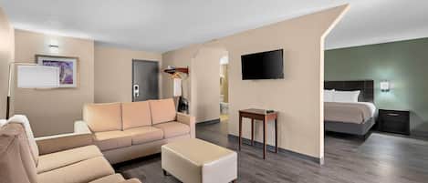 A modern hotel room with a sofa, ottoman, flat-screen TV, bedside table, and a bed.