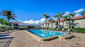 A pool area with a brick patio, lounge chairs, and palm trees.