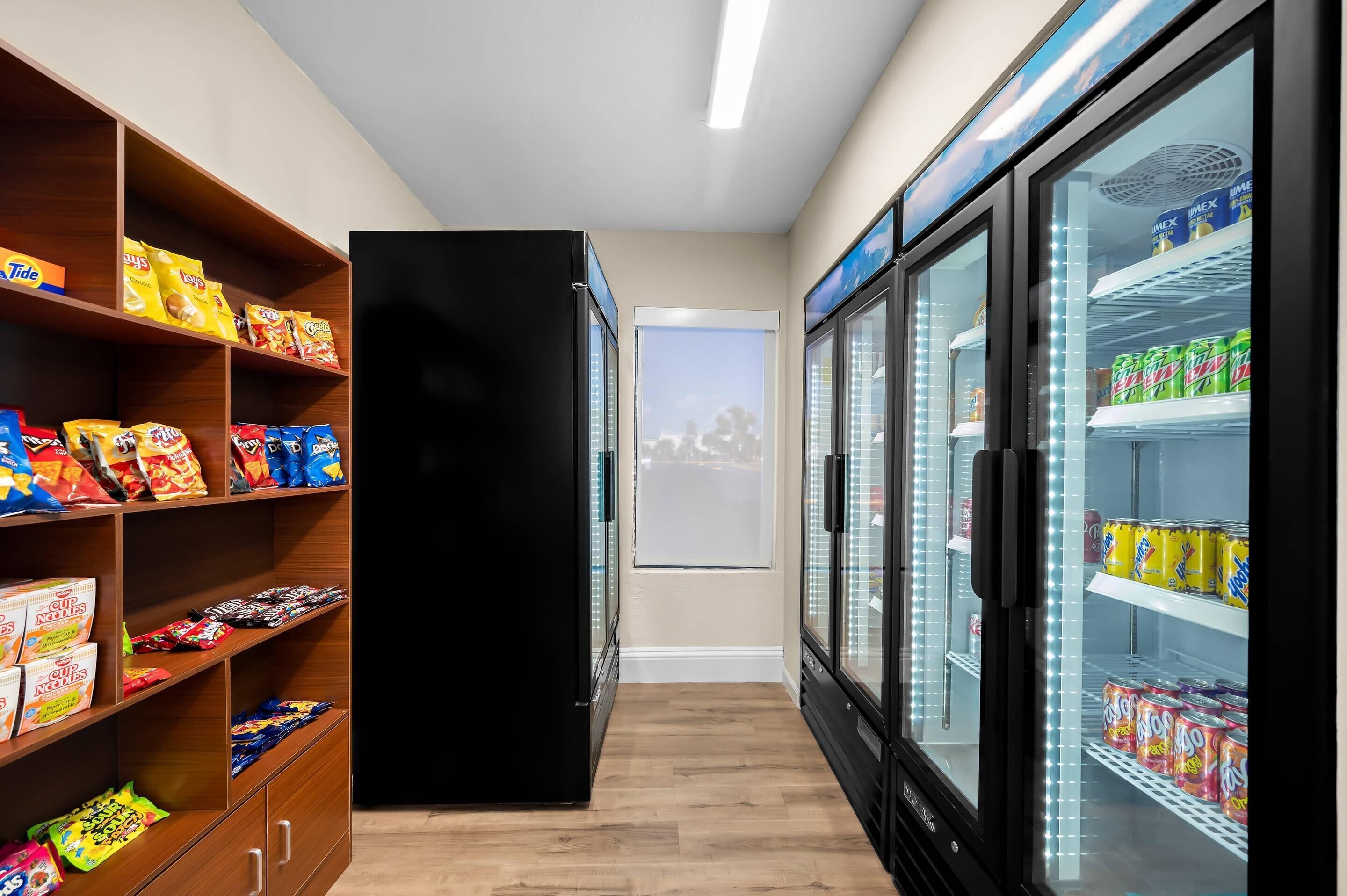 A corridor with snack shelves, a black refrigerator, and a refrigerated display with beverages.
