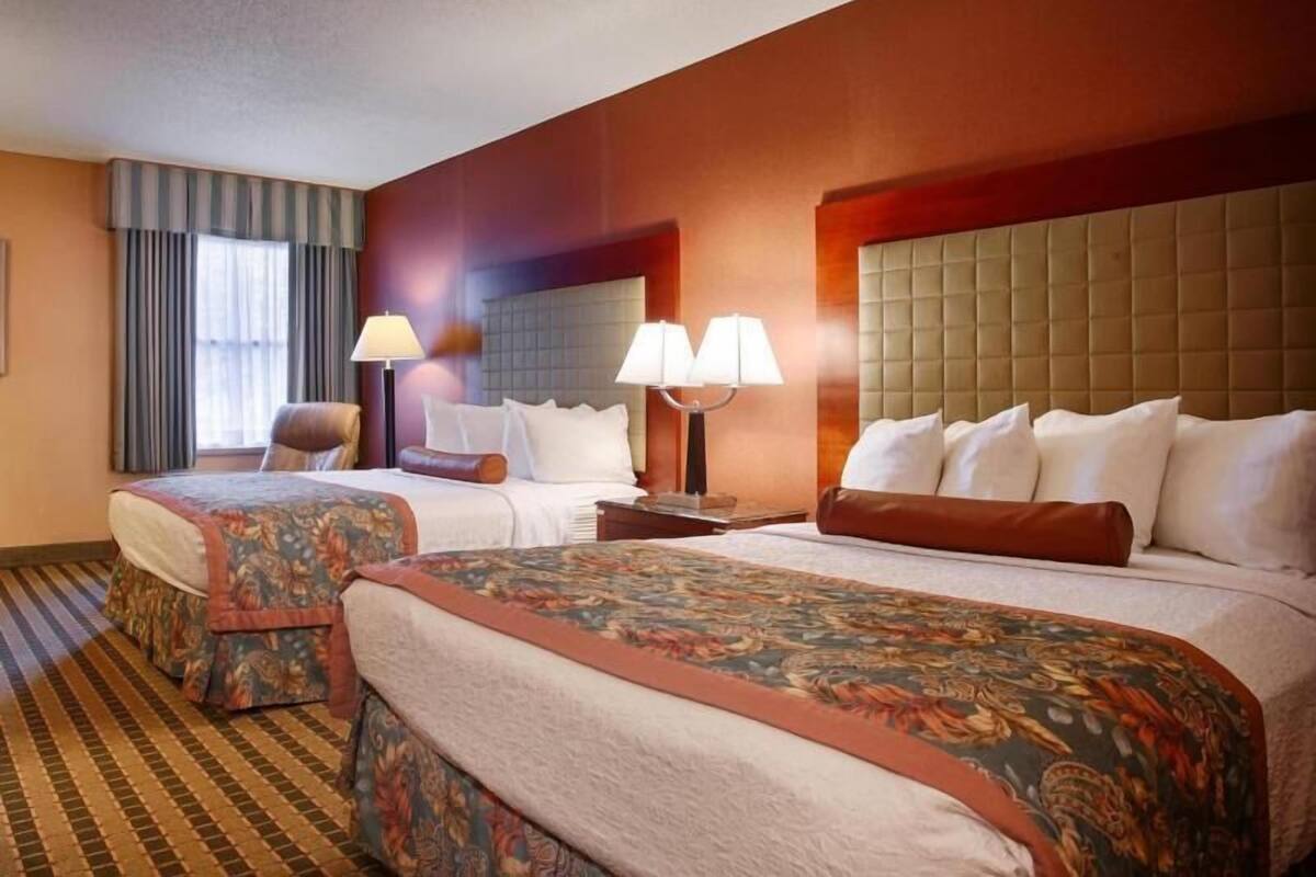 Habitación de hotel con dos camas, un ventanal con cortinas, cabecera y lámpara.