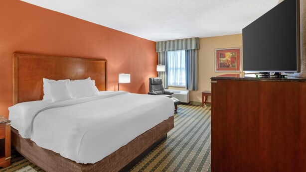 A hotel room with a large bed, a desk, a chair, and a television.