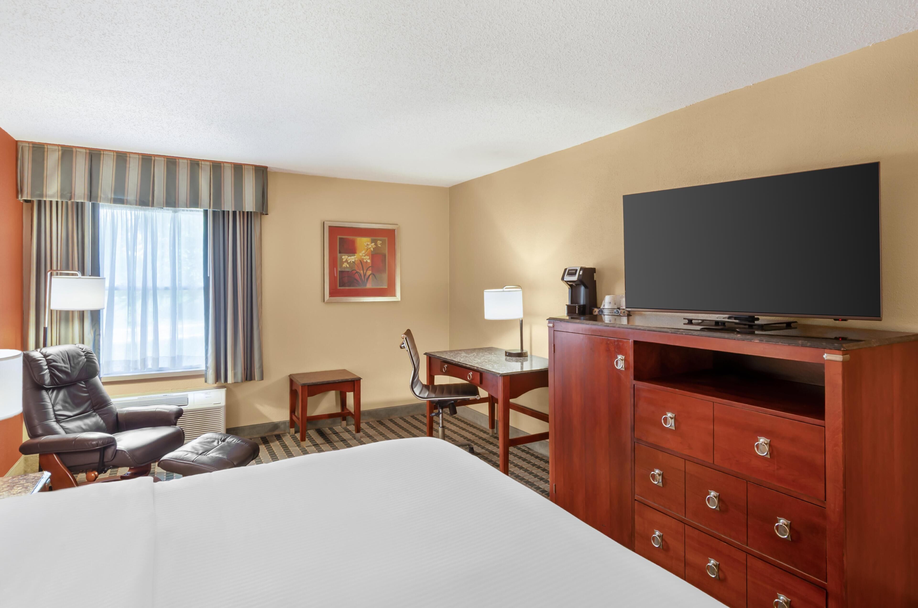 A hotel room with a bed, a desk, a chair, a television, and a window with curtains.