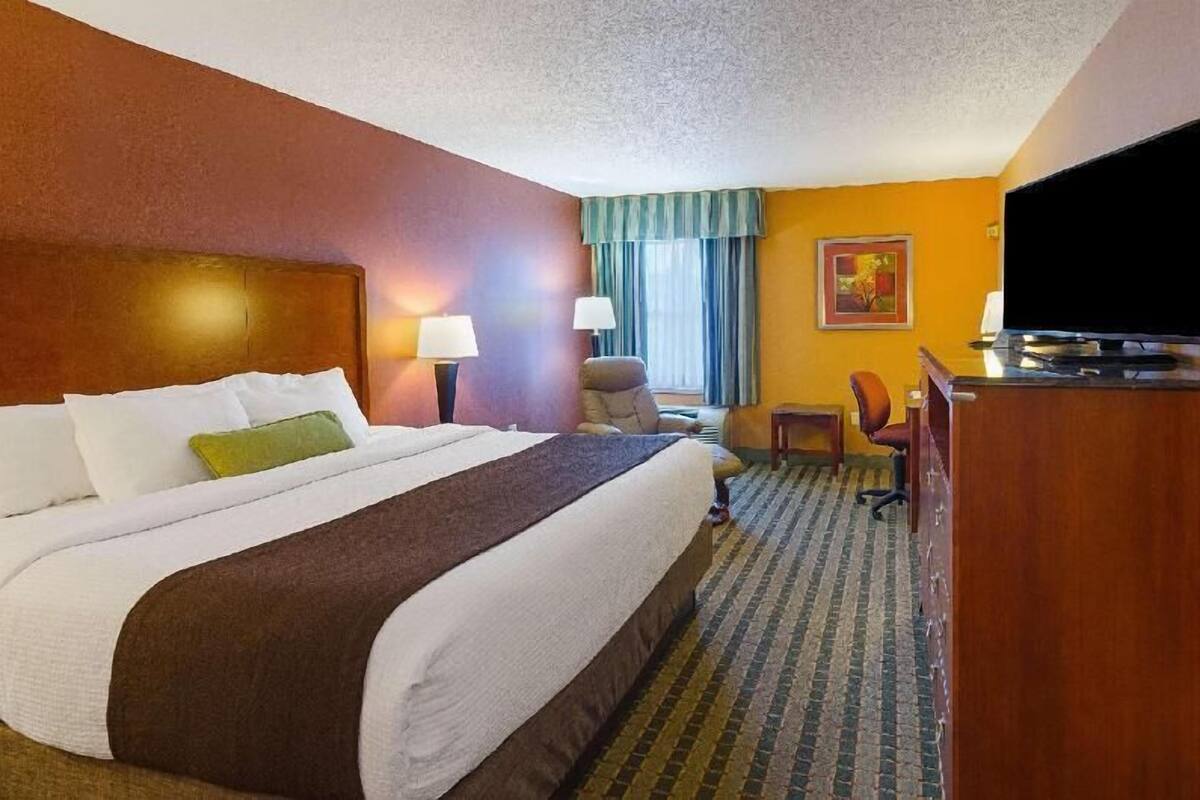 Una habitación de hotel con una cama grande, un escritorio, una silla, un televisor y una ventana con cortinas.