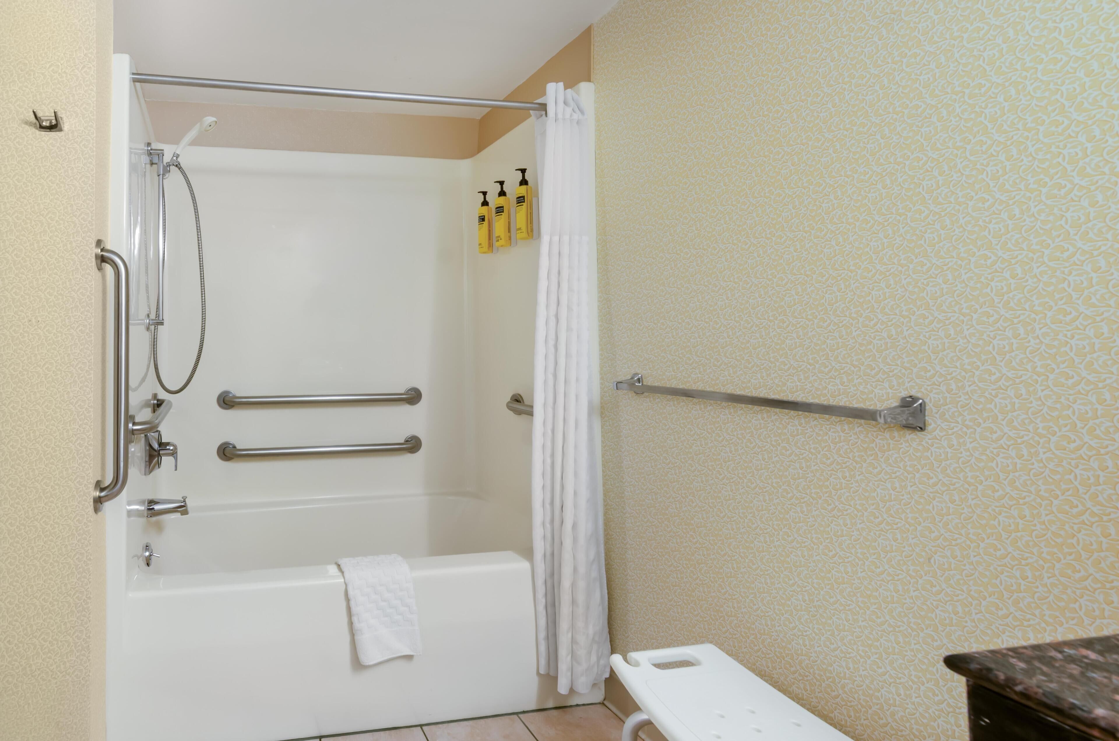 A bathroom with a bathtub, a shower, a towel rack, and a handrail.