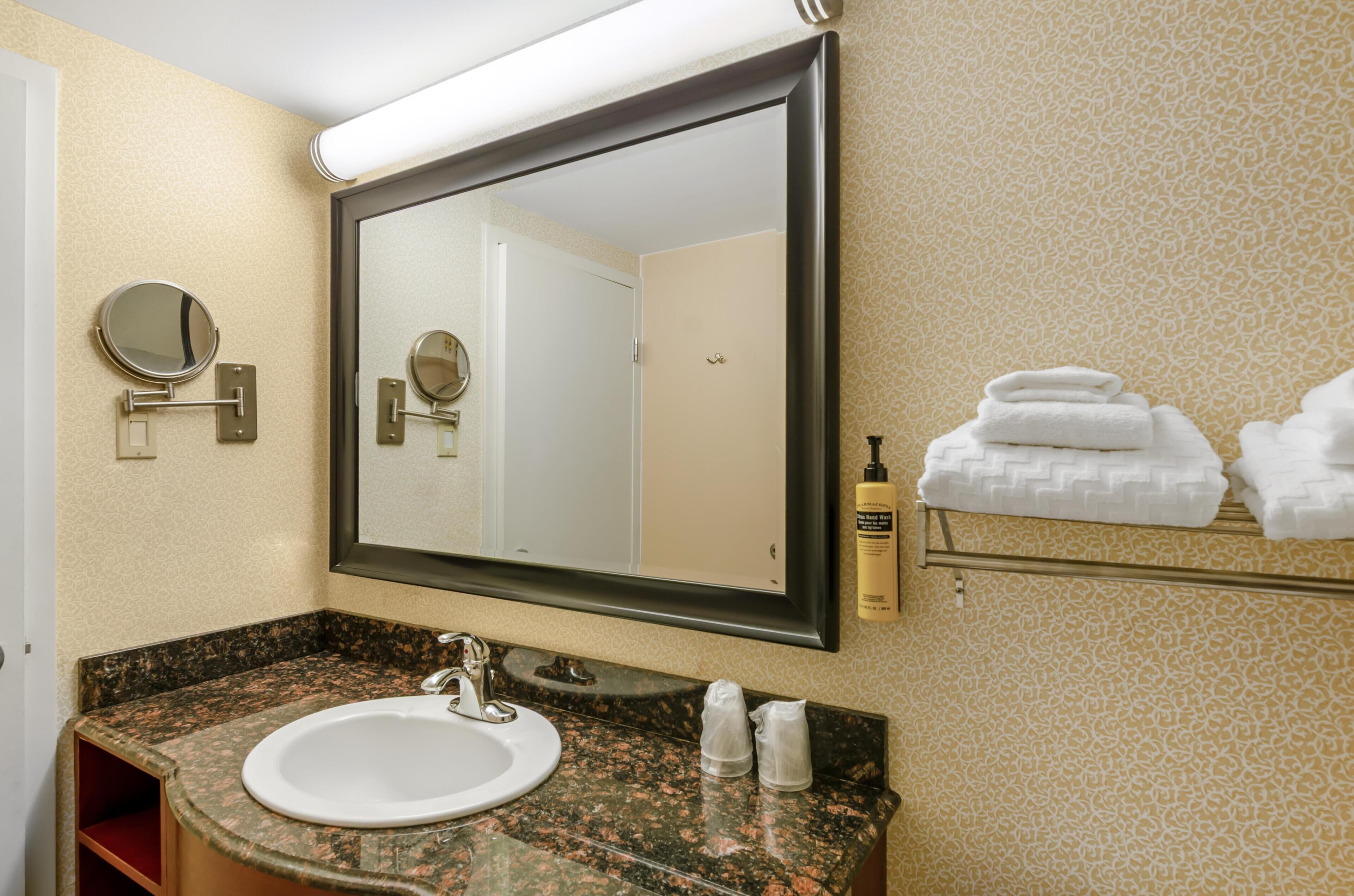 A bathroom with a sink, two mirrors, a towel rack with towels, and toiletries.