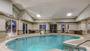 An indoor swimming pool with a tiled deck, a metal ladder, and a view of the outside.