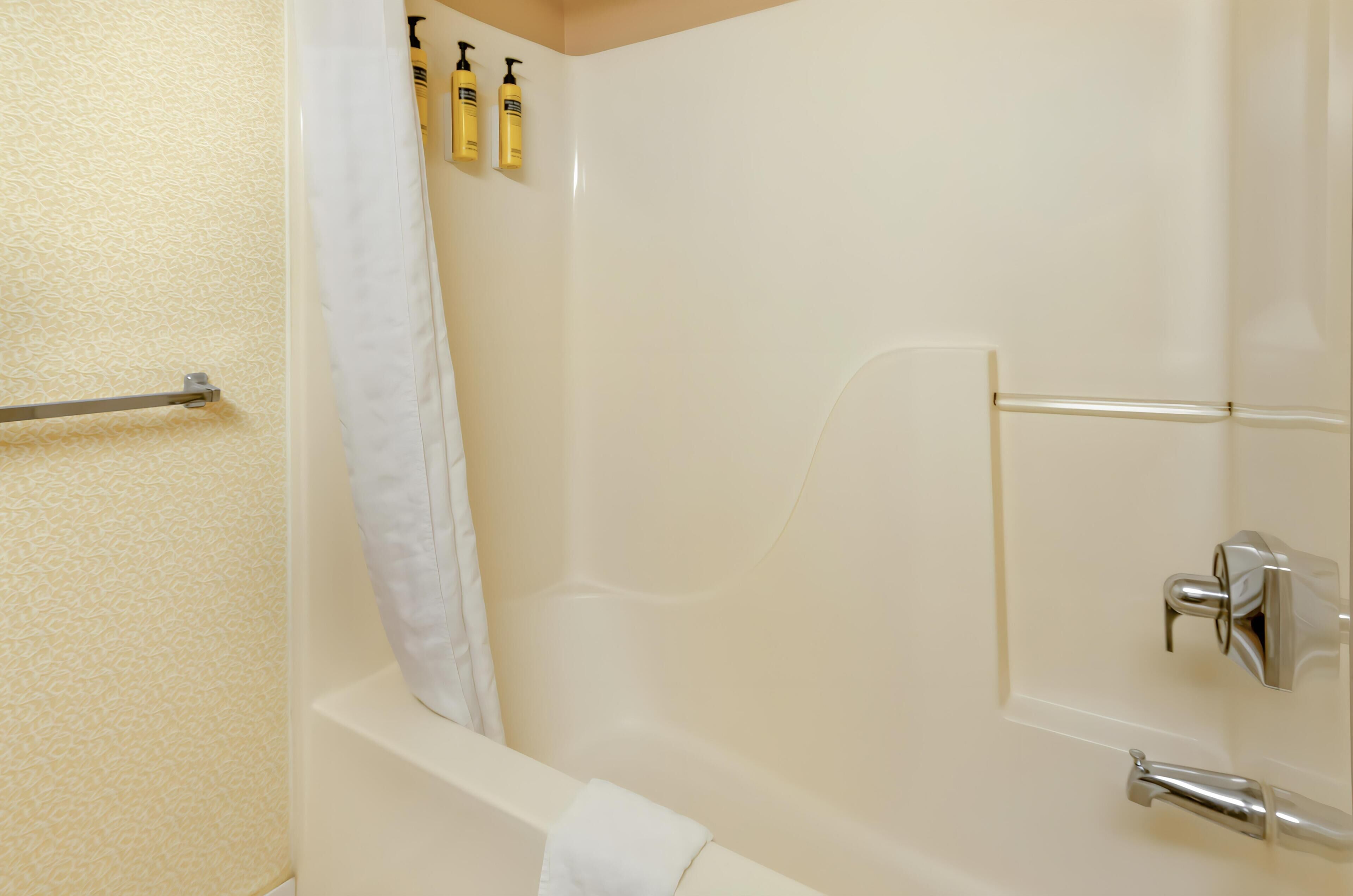 A bathroom with a bathtub, a shower curtain, and two bottles of shampoo on the wall.