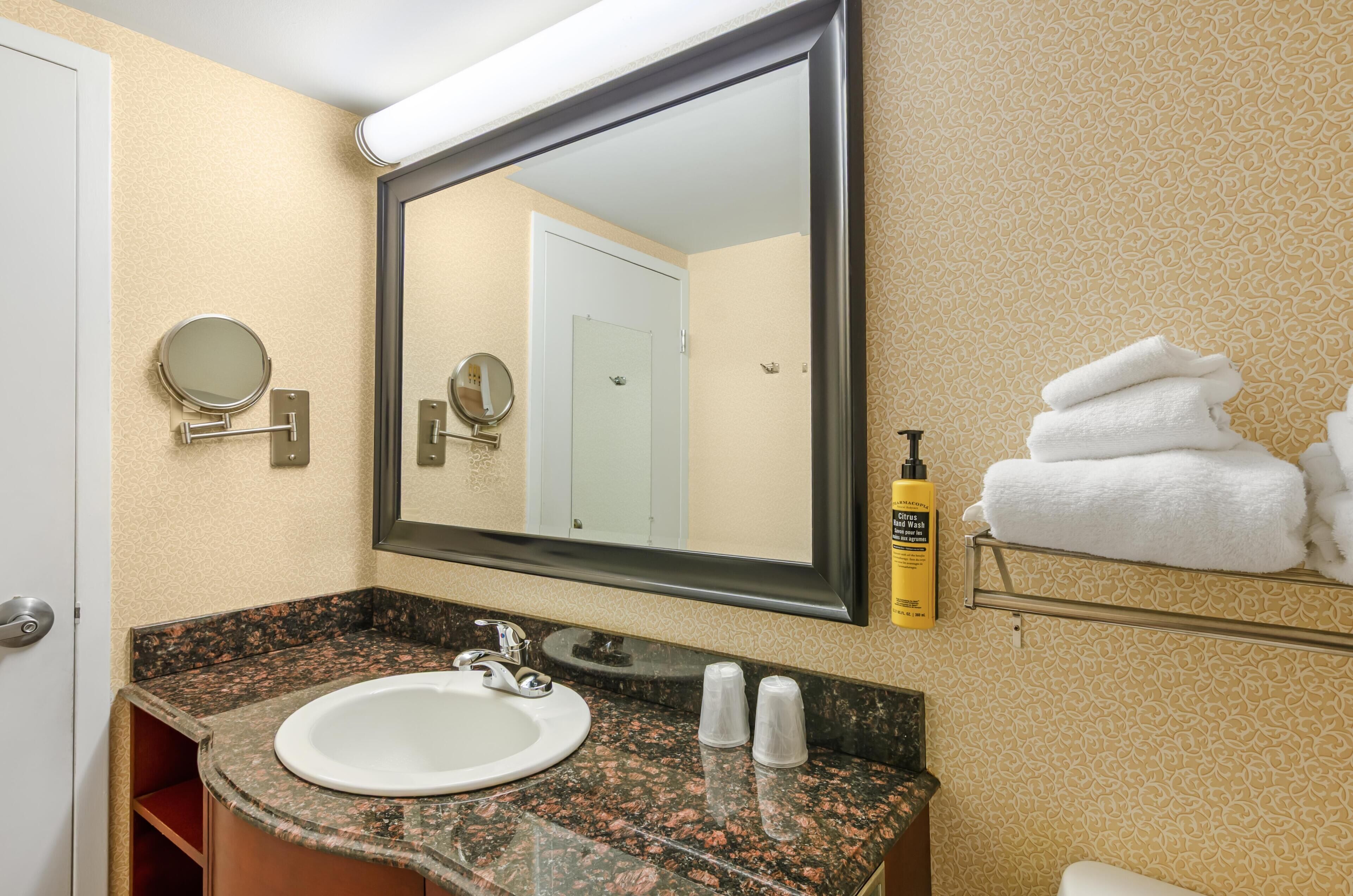 A bathroom with a sink, mirror, towel rack, and toiletries.