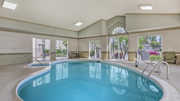 A large indoor swimming pool with clear glass walls, a metal ladder, and a view of the outside. - Best Western Plus Inn at Valley View (Roanoke)