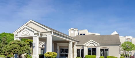 A hotel with a covered entrance, multiple windows, and a parking lot.