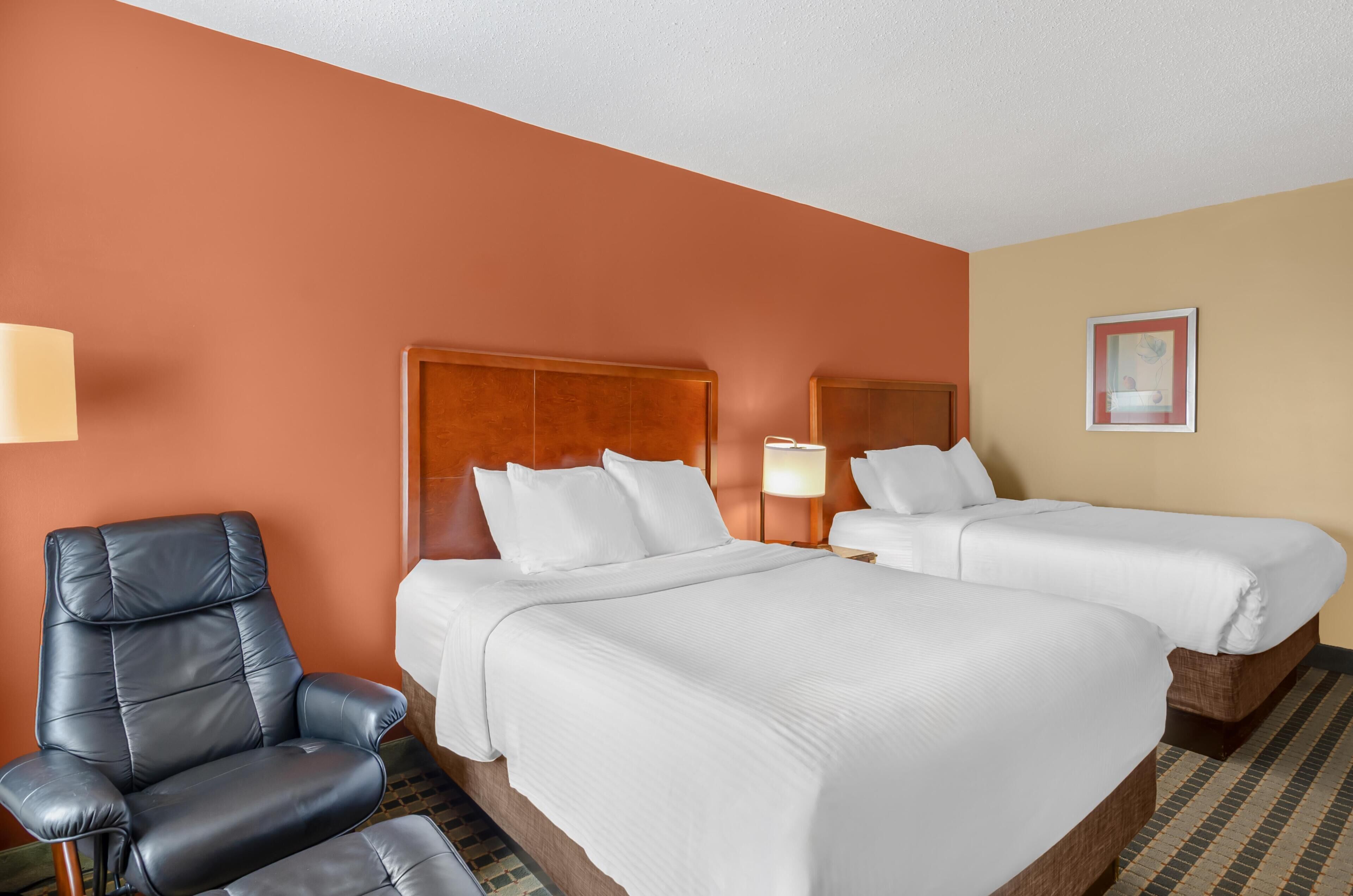 A hotel room with two beds, a black leather chair, and a lamp.