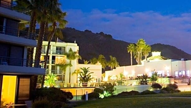 A hotel with multiple floors, palm trees, and a mountain in the background. - The Cliffs Hotel and Spa (Pismo Beach)