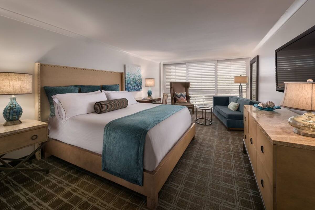 Ein Hotelzimmer mit einem großen Bett, einem Schreibtisch, einem Sessel, einer Couch und einem Fernseher.