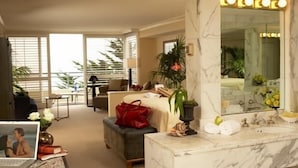 A hotel room with a large mirror, a marble bathroom vanity, a sofa, and a dining area with a table and chairs. - The Cliffs Hotel and Spa (Pismo Beach)