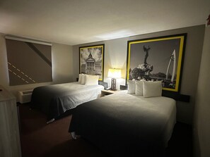Una habitación de hotel con dos camas, un escritorio, una lámpara y dos cuadros en la pared.