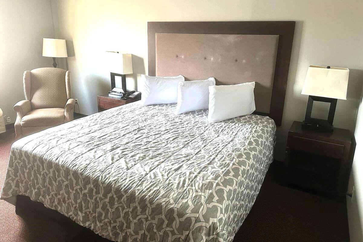 A hotel room with a large bed, two bedside tables, a chair, and lamps.