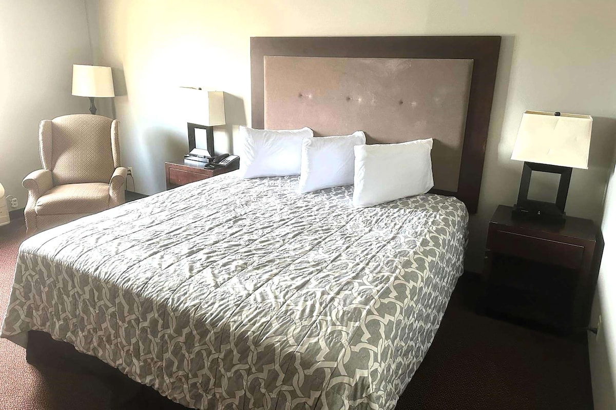 A hotel room with a large bed, two bedside tables, a chair, and lamps.