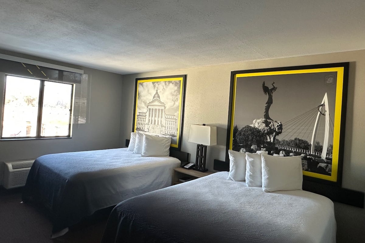 A hotel room with two beds, a window with a view, and two framed pictures on the wall.