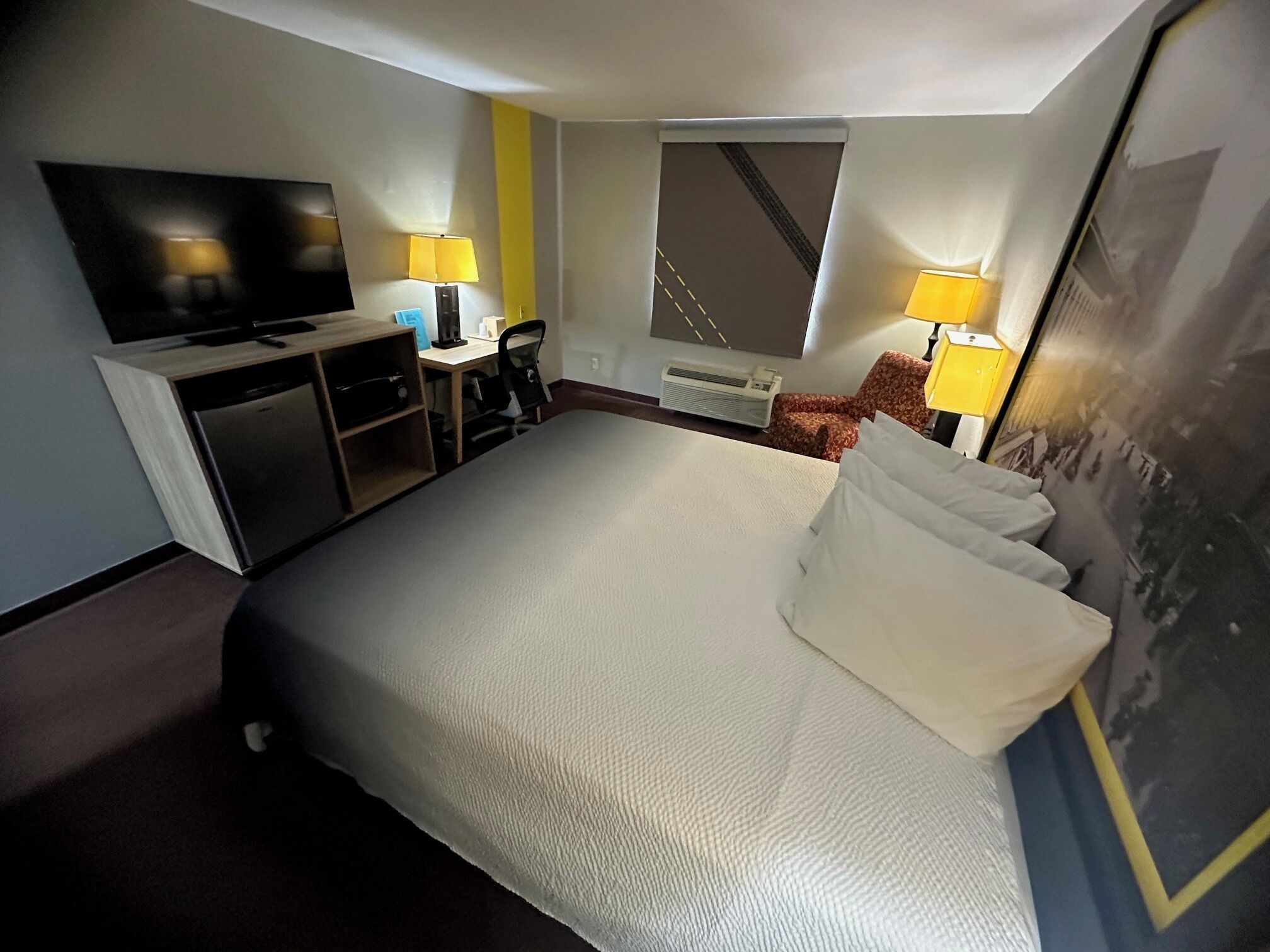 A hotel room with a bed, a desk with a chair, a television, and two lamps.