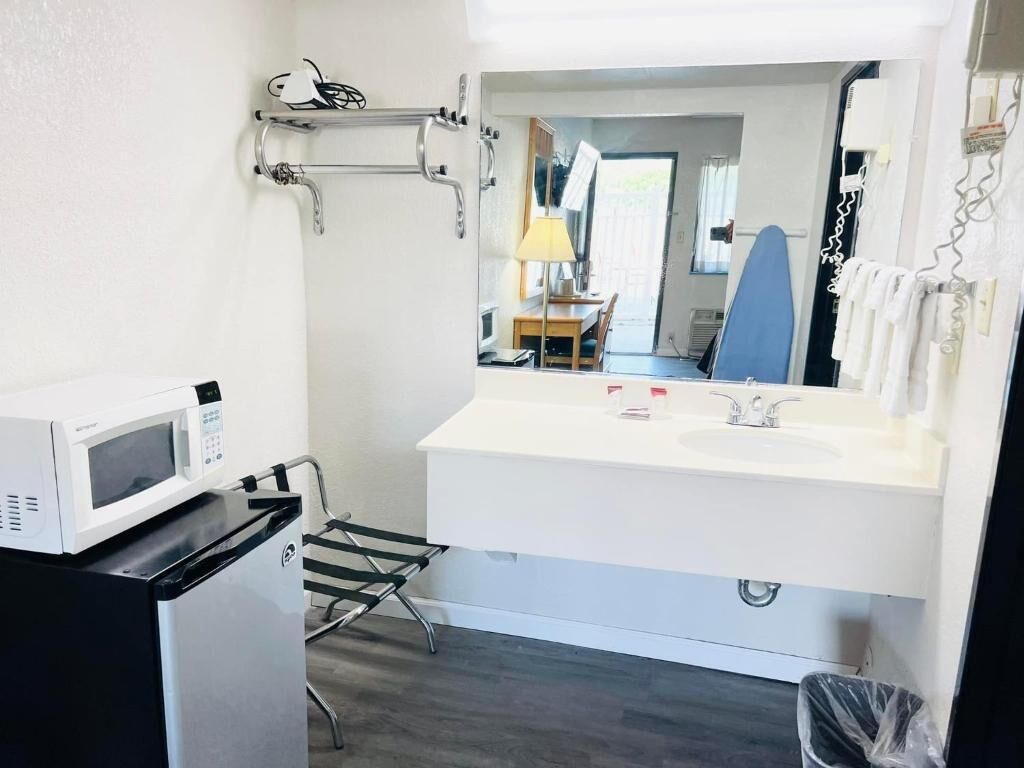 A compact bathroom with a white sink, a mirror, a microwave, and a small trash bin.
