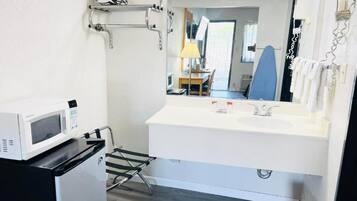 Un baño pequeño con un lavamanos blanco, un espejo, un microondas y un bote de basura.