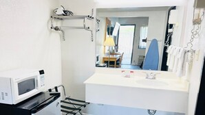A compact hotel bathroom with a white sink, a mirror, a microwave, and a small table with a chair. - Super 8 by Wyndham Fort Scott (Fort Scott)