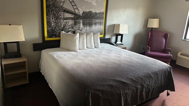 A hotel room with a large bed, two bedside tables with lamps, a chair, and a large framed picture of a bridge over water. - Super 8 by Wyndham Fort Scott (Fort Scott)