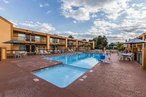 A hotel pool area with a rectangular pool, lounge chairs, and umbrellas.