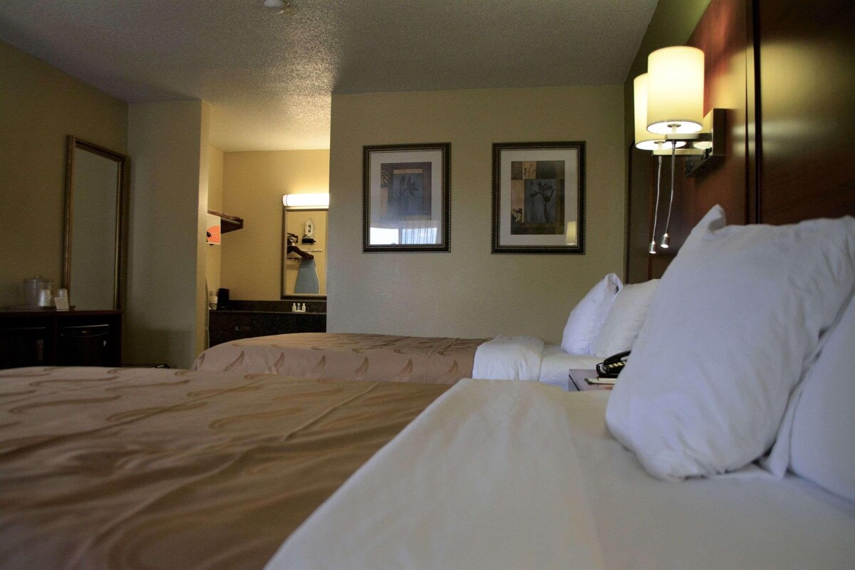 A hotel room with two beds, a large mirror, and framed artwork on the wall.