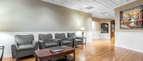 A spacious lobby with a wooden floor, a row of grey upholstered chairs, a wooden coffee table, and a painting on the wall.