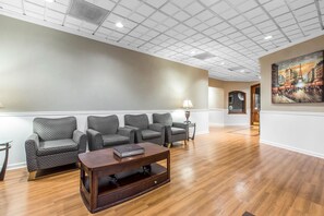 A spacious lobby with a wooden floor, a row of grey upholstered chairs, a wooden coffee table, and a painting on the wall.