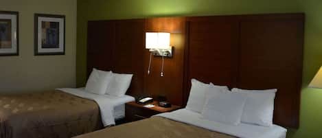 A hotel room with two beds, a nightstand, a lamp, and framed pictures on the wall.
