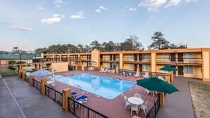 A hotel with a swimming pool, outdoor seating, and a multi-story building.