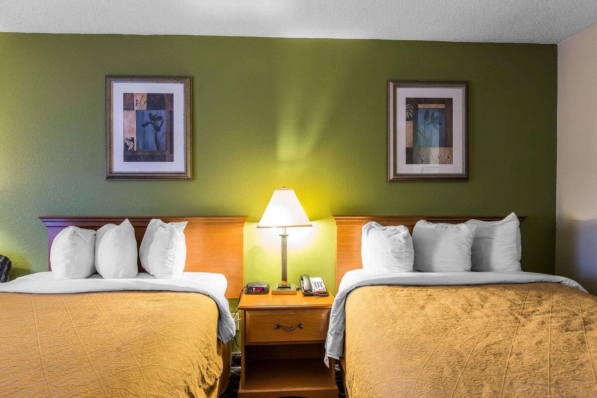 A hotel room with two beds, a nightstand with a lamp, a phone, and two framed pictures on the wall.