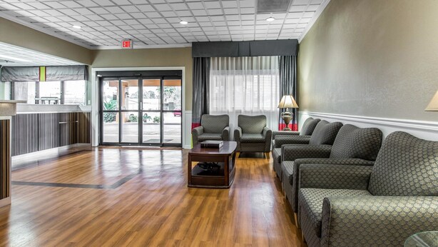 A hotel lobby with a wooden floor, seating area with sofas and armchairs, a reception desk, and a view of the outside through large windows.
