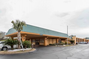 A hotel with a green roof and orange facade, featuring a covered entrance and palm trees in the foreground.