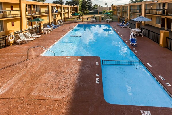 Una piscina con sillas de descanso y sombrillas, rodeada de edificios hoteleros de varios pisos.