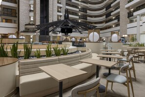 A modern indoor seating area with a curved sofa and tables, surrounded by potted plants and a central water feature. - Embassy Suites by Hilton Orlando International Drive ICON Park (Orlando)
