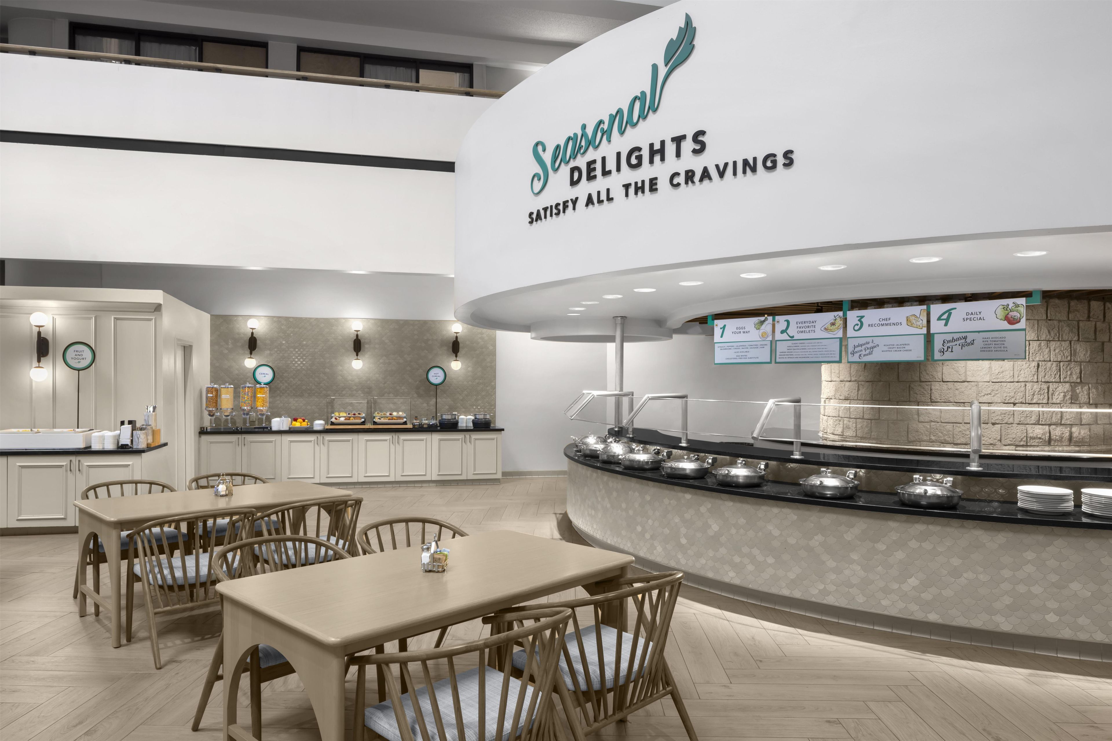 A modern breakfast area with a counter displaying food options and a seating area with tables and chairs.