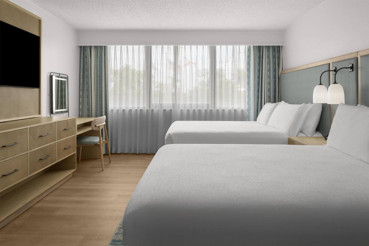 A hotel room with two beds, a desk, a TV, and a window with curtains.