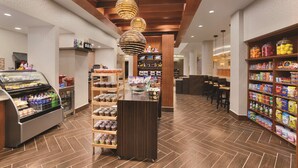 A hotel lobby with a deli counter, snack shelves, and a seating area.