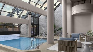 An indoor swimming pool with a glass ceiling, lounge area with seating, and a stone wall.