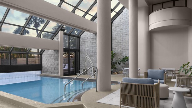 An indoor swimming pool with a glass ceiling, lounge area with seating, and a stone wall. - Embassy Suites by Hilton Orlando International Dr ICON Park (Orlando)