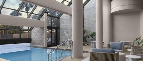 Une piscine intérieure dotée d’un toit en verre, un espace détente avec des sièges et un mur en pierre.