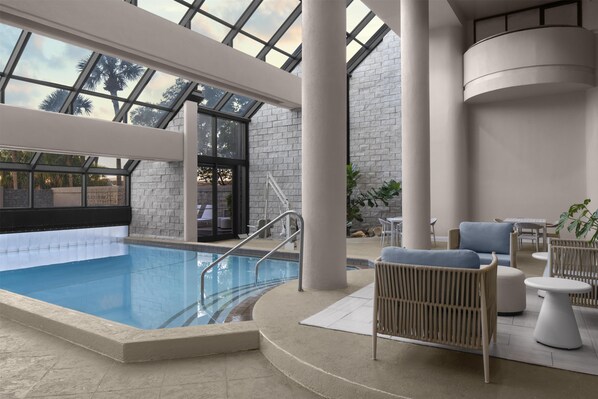 An indoor swimming pool with a glass ceiling, lounge area with seating, and a stone wall. - Embassy Suites by Hilton Orlando International Dr ICON Park (Orlando)