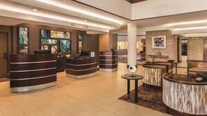 A reception area with a 'RECEPTION' sign, multiple reception desks, a seating area with a round table, and a wall with framed pictures.