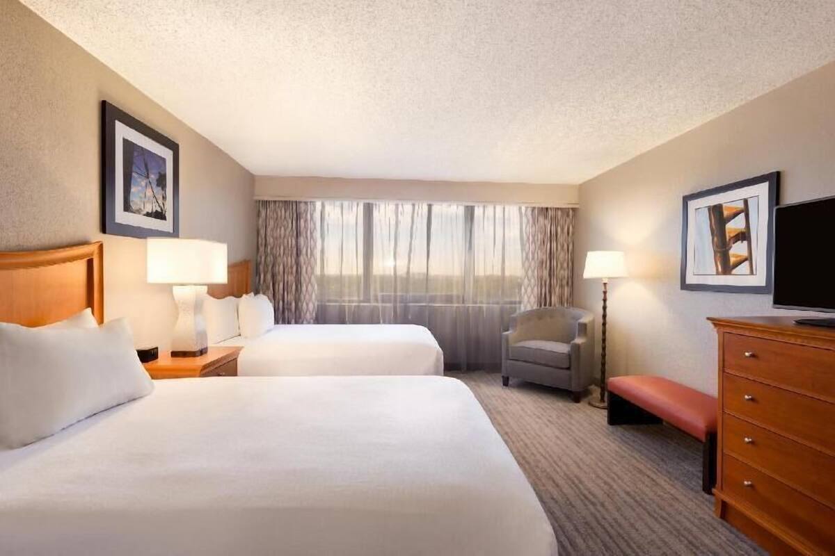 A hotel room with two beds, a desk, a chair, a television, and a window with curtains.