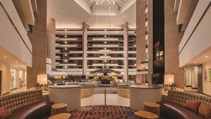 A spacious lobby with a high ceiling, multiple floors of residential units, and a central seating area with round tables and sofas.